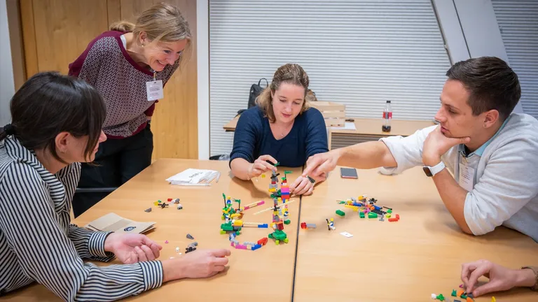 Four people sitting at a table collaboratively building an abstract lego structure